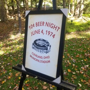 May include: A framed sign with the text "10&cent; BEER NIGHT JUNE 4, 1974 CLEVELAND, OHIO MUNICIPAL STADIUM" and a black and white illustration of a stadium.
