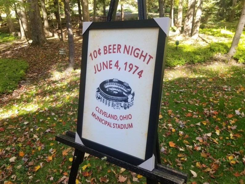 May include: A framed sign with the text "10&cent; BEER NIGHT JUNE 4, 1974 CLEVELAND, OHIO MUNICIPAL STADIUM" and a black and white illustration of a stadium.