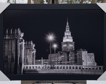 Pode incluir: Fotografia a preto e branco da Terminal Tower em Cleveland, Ohio, à noite. A torre está iluminada e as luzes refletem-se nas janelas. A fotografia foi tirada de uma ponte olhando para a torre.