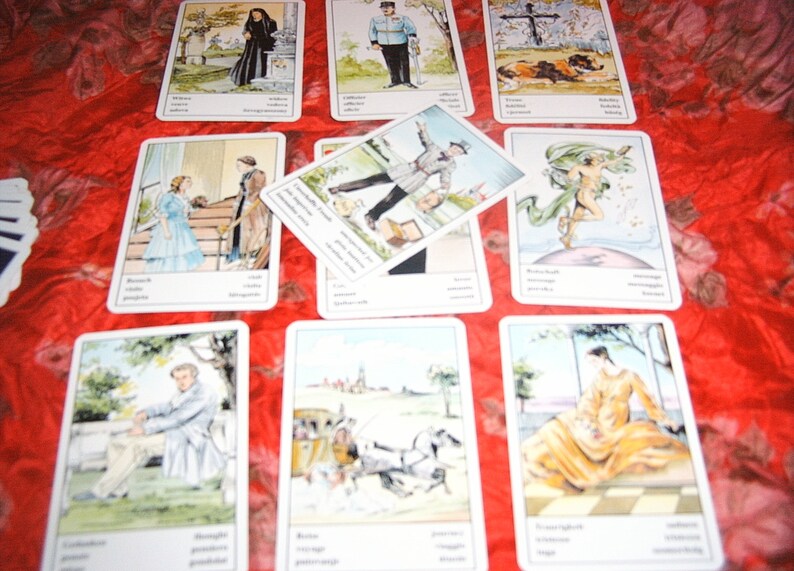 Pu&ograve; includere: Un insieme di carte dei tarocchi con illustrazioni e testo. Le carte presentano varie scene, tra cui figure in abiti storici, paesaggi e immagini simboliche. Le carte sono disposte su una superficie rossa a motivi.