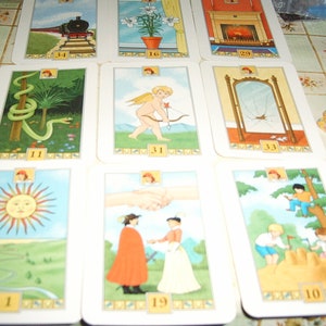 Pu&ograve; includere: Un mazzo di carte dei tarocchi con illustrazioni colorate. Le carte raffigurano varie scene, tra cui un treno, un serpente, un angelo con arco e frecce, uno specchio rotto, una stretta di mano e bambini che giocano. Ogni carta &egrave; numerata.