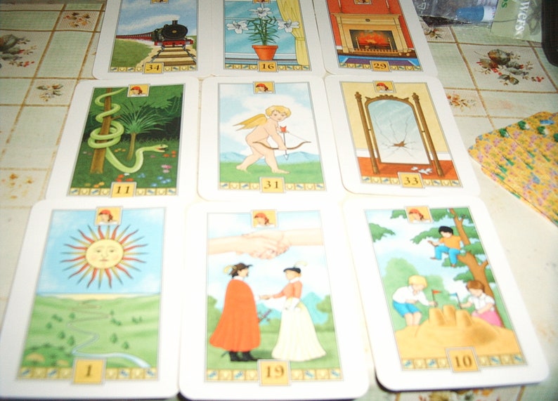 Pu&ograve; includere: Un mazzo di carte dei tarocchi con illustrazioni colorate. Le carte raffigurano varie scene, tra cui un treno, un serpente, un angelo con arco e frecce, uno specchio rotto, una stretta di mano e bambini che giocano. Ogni carta &egrave; numerata.