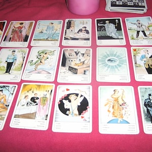 Pu&ograve; includere: Un insieme di carte dei tarocchi disposte su una superficie rosa. Ogni carta presenta un'illustrazione unica con testo. Le carte raffigurano varie scene e figure, con un'estetica vintage. Un contenitore rosa e un mazzo di carte sono visibili sullo sfondo.
