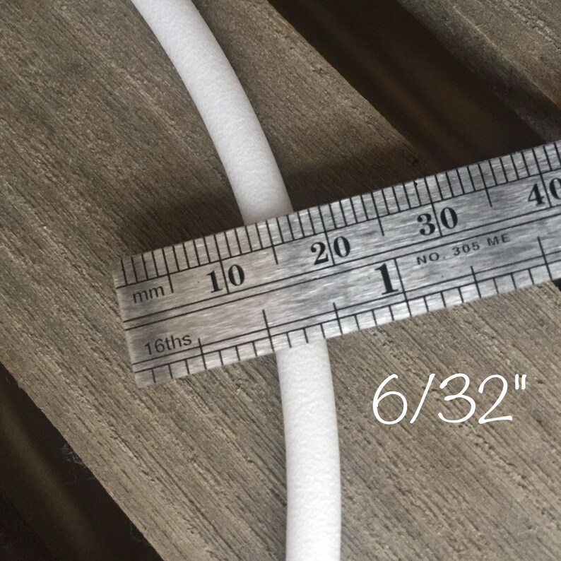 May include: A white, cylindrical foam tube is measured with a metal ruler. The ruler shows the tube is 6/32 inches in diameter. The tube is positioned on a wooden surface.