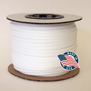 May include: A spool of white elastic cord. The cord is tightly wound around a cardboard core. A sticker with the text "MADE IN USA" and an American flag is visible.