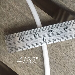 May include: A close-up of a white, cylindrical object being measured with a ruler. The ruler shows measurements in millimeters and 16ths of an inch. The text "4/32" is written below the object, indicating its size.