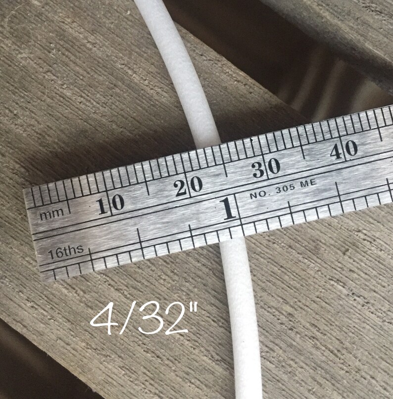 May include: A close-up of a white, cylindrical object being measured with a ruler. The ruler shows measurements in millimeters and 16ths of an inch. The text "4/32" is written below the object, indicating its size.