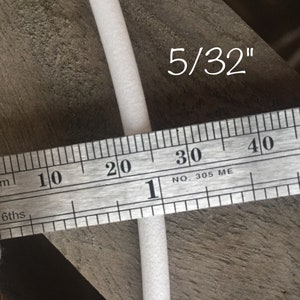 May include: A close-up of a white foam rod, approximately 5/32 inches in diameter, is measured with a metal ruler. The ruler displays both inch and centimeter markings. The text "5/32" is written in white.