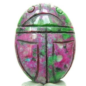 May include: A carved green and pink gemstone scarab beetle pendant. The beetle is carved in detail and has a smooth, polished finish.