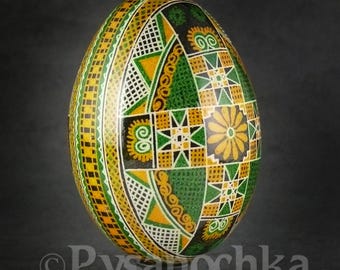 Puede incluir: Un huevo de Pascua ucraniano tradicional, llamado pysanka, de color verde, amarillo y blanco, con un diseño geométrico. El huevo está decorado con intrincados patrones y espirales.