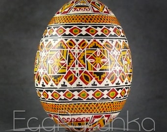 May include: A hand-painted Easter egg with a geometric pattern in red, black, yellow, and white. The egg is on a black stand.