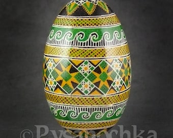 May include: A hand-painted Easter egg with a geometric pattern in shades of green, yellow, black, and white. The egg is on a stand and has a glossy finish.