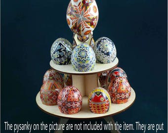 Könnte beinhalten: Ein Holzständer mit zwei Ebenen, auf dem eine Sammlung von aufwendig bemalten Pysanka-Eiern ausgestellt ist. Die Eier sind mit bunten geometrischen Mustern und Designs verziert.