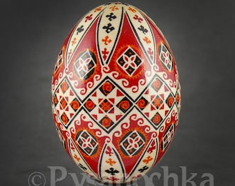 May include: A red, black, and white decorated Easter egg with a geometric pattern. The egg is on a black stand.