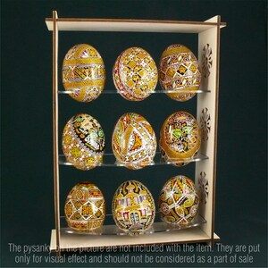 Puede incluir: Soporte de madera con tres estantes para exhibir ocho huevos de Pascua decorados. Los huevos est&aacute;n pintados en varios colores y patrones, incluyendo rojo, amarillo, negro y blanco.