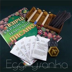 May include: A kit for creating Ukrainian pysanky eggs, featuring a book with instructions, wooden tools, wax for outlining designs, and dye packets in yellow, red, light blue, and black.