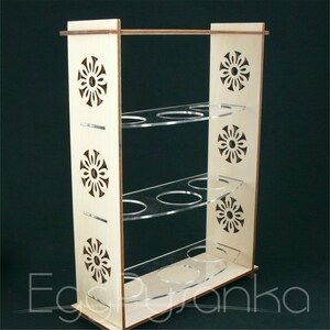 Puede incluir: Un soporte para huevos de madera con tres estantes y un dise&ntilde;o floral decorativo. Los estantes son de acr&iacute;lico transparente.