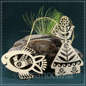 May include: Three wooden ornaments with a folk art design. The ornaments are shaped like a bird, a house, and a fish. Each ornament features a stylized bird with a flower and leaves.