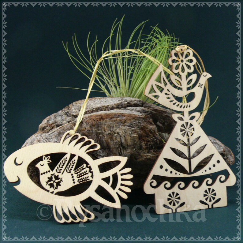 May include: Three wooden ornaments with a folk art design. The ornaments are shaped like a bird, a house, and a fish. Each ornament features a stylized bird with a flower and leaves.