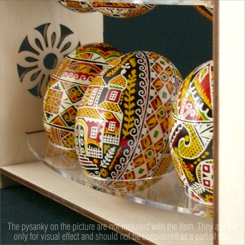 Puede incluir: Un expositor de madera con un estante de acr&iacute;lico transparente para exhibir huevos decorativos. Los huevos est&aacute;n pintados con intrincados patrones en rojo, amarillo, negro y blanco.