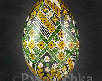 May include: A green, yellow, and white pysanka, a Ukrainian Easter egg, with a geometric pattern and floral accents.