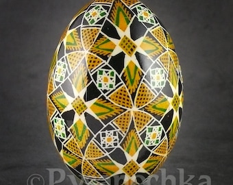 May include: A black, white, gold, and green decorated Easter egg with a geometric pattern. The egg is on a stand.