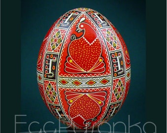 May include: A decorative, hand-painted egg with a vibrant red background. The egg features intricate patterns in black, white, and yellow, including a stylized bird design. The word "Eggyranka" is written on the bottom of the egg.