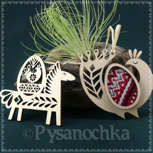 May include: Three wooden ornaments in the shape of a horse, a bird, and an egg. The horse and bird have intricate cutouts and the egg has a red and white embroidered design. The ornaments are all hanging from a string.
