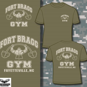 May include: Olive green t-shirts with the text "FORT BRAGG GYM" and a weightlifting graphic. One shirt shows the design on the front and back, and the other shows the design on the front. The text "FAYETTEVILLE, NC" is also included.