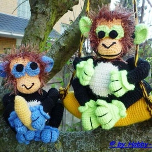 May include: Two crocheted monkey toys, one holding a banana and the other sitting on a yellow crocheted swing. The monkey on the swing has green eyes and a white face. The monkey holding the banana has blue eyes and a black and white face.