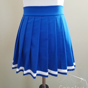 May include: A royal blue pleated skirt with a white trim around the bottom. The skirt is on a white mannequin.