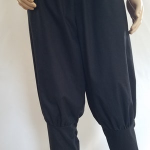 May include: Black cotton pants with a gathered detail at the ankles. The pants have a wide leg and a relaxed fit.