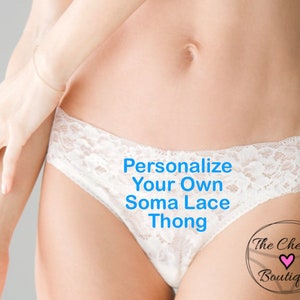 May include: A white lace thong featuring a floral pattern. The text 'Personalize Your Own Soma Lace Thong' is printed in blue across the front. A circular logo in the bottom right corner reads 'The Cheeky Boutique' with a small pink heart icon.