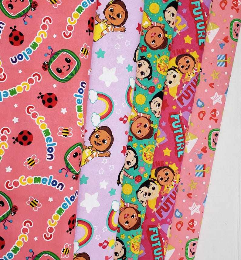 Peut inclure: Plusieurs rouleaux de tissu color&eacute;s avec des motifs Cocomelon. Les motifs incluent des past&egrave;ques, des coccinelles, des arcs-en-ciel, des &eacute;toiles et le mot "FUTURE". Les tissus sont dans des tons de rose, de violet et de vert.