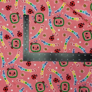 Peut inclure: Tissu rose avec un motif r&eacute;p&eacute;t&eacute; de personnages de t&eacute;l&eacute;vision en forme de past&egrave;que, de coccinelles, d'abeilles et d'&eacute;toiles. Le mot "Cocomelon" est &eacute;crit dans une police incurv&eacute;e. Id&eacute;al pour les projets pour enfants.