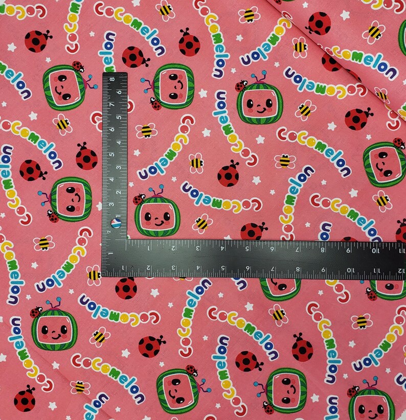 Peut inclure: Tissu rose avec un motif r&eacute;p&eacute;t&eacute; de personnages de t&eacute;l&eacute;vision en forme de past&egrave;que, de coccinelles, d'abeilles et d'&eacute;toiles. Le mot "Cocomelon" est &eacute;crit dans une police incurv&eacute;e. Id&eacute;al pour les projets pour enfants.