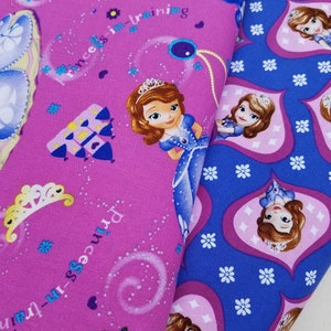 May include: Pink and blue fabric with a princess theme. The fabric features a repeating pattern of a princess with brown hair wearing a blue dress, a castle, and the text "Princess-in-training".
