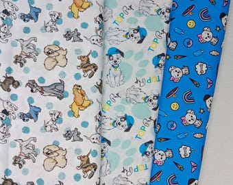 May include: Three vertical strips of fabric featuring dog-themed patterns. The left strip is white with various dog breeds and blue dots. The centre strip is white with Dalmatian puppies wearing blue hats and the text Top Pup. The right strip is blue.