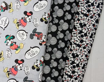 May include: Three fabric panels featuring Mickey Mouse and Minnie Mouse. The first panel is gray with a white background and features Mickey and Minnie in various poses with speech bubbles that say "Let's Go", "So Much To See", and "So Little Time". The second panel is black with a white background and features a repeating pattern of Mickey Mouse's head. The third panel is black with a white background and features a repeating pattern of Mickey Mouse's face.