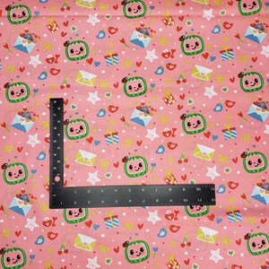 Peut inclure: Tissu rose avec un motif r&eacute;p&eacute;t&eacute; de tranches de past&egrave;que souriantes avec des coccinelles, des enveloppes, des cadeaux, des &eacute;toiles, des coeurs et des oiseaux. Une r&egrave;gle noire est plac&eacute;e sur le tissu. Id&eacute;al pour les loisirs cr&eacute;atifs ou les v&ecirc;tements pour enfants.