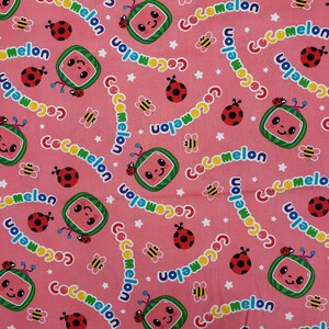 Peut inclure: Tissu rose avec un motif r&eacute;p&eacute;t&eacute; de tranches de past&egrave;que souriantes, de coccinelles, d'abeilles, d'&eacute;toiles et le mot "Cocomelon". Parfait pour les cr&eacute;ations et v&ecirc;tements pour enfants.