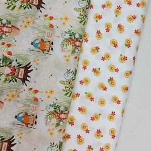 May include: Two fabric rolls. One features a repeating pattern of garden gnomes, flowers, and strawberries on a cream background. The other has a white background with a pattern of yellow and red flowers.