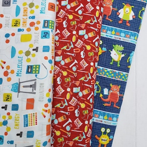 May include: Three different fabric panels with a science theme. The first panel is white with a red, yellow, and blue science pattern. The second panel is red with a white, yellow, and blue science pattern. The third panel is blue with a white, yellow, and orange monster pattern. The text on the panels includes "Molecule", "Ionic Bond", "Energy", "Equation", "Joule", "Ne", "360 F", and "300 F".