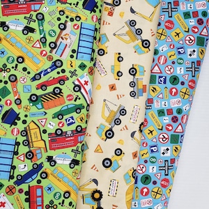 May include: Three rolls of fabric with transportation-themed patterns. One roll features a green background with cars, buses, and road signs. Another has a beige background with construction vehicles. The third has a blue background with road signs.