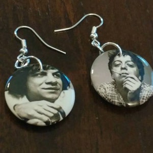 May include: A pair of earrings featuring round button-shaped charms with black and white photos of a person. The earrings are silver and have a hook closure.