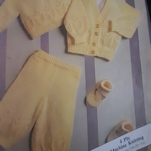 Puede incluir: Un conjunto de ropa de punto amarillo para bebé que incluye un cárdigan, una camiseta, pantalones y botines. El conjunto está hecho con hilo de punto de máquina de 4 cabos. El texto de la etiqueta dice "4 Ply Machine Knitting 40-50 cms (16-20 ins)"