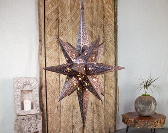 May include: A large, rustic, metal star-shaped pendant light with a distressed copper finish. The light has a cutout design and is illuminated with warm white lights.