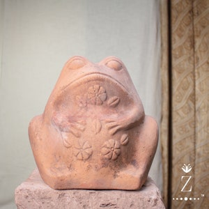 Może przedstawiać: Figurkę żaby z terakoty z detalicznym wzorem kwiatów i liści. Żaba siedzi z podkurczonymi nogami i ma zaokrągloną, gładką powierzchnię.