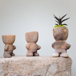 May include: A set of three ceramic mugs with a speckled, matte finish. The mugs are in shades of cream, light gray, and dark gray. Each mug has a simple, minimalist design, perfect for coffee or tea.