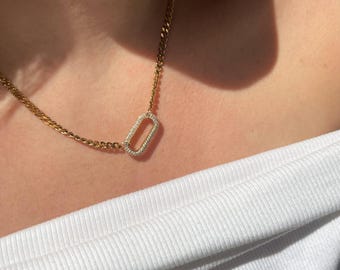 May include: A gold chain necklace with a rectangular pendant set with small clear stones.